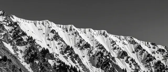 Black and white view of a knife-edge snow cornice mountain ridge under a moody dark sky