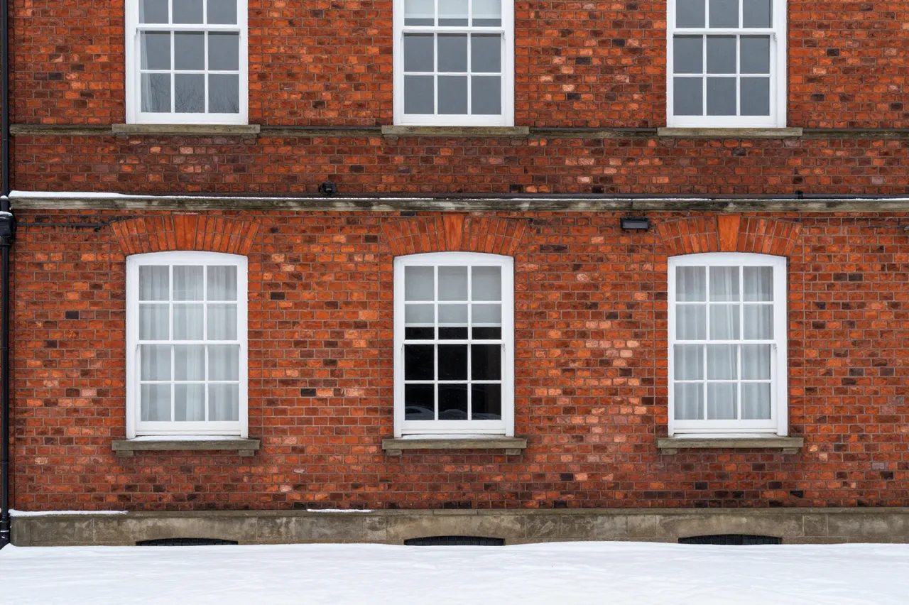 Symmetrical white-framed windows on a red brick Georgian house above fresh fallen snow