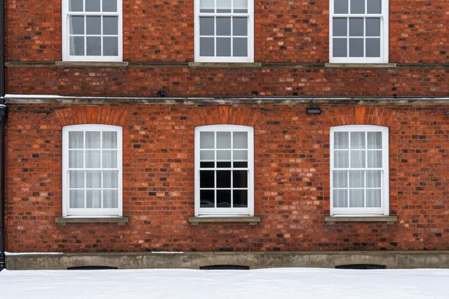 Symmetrical white-framed windows on a red brick Georgian house above fresh fallen snow