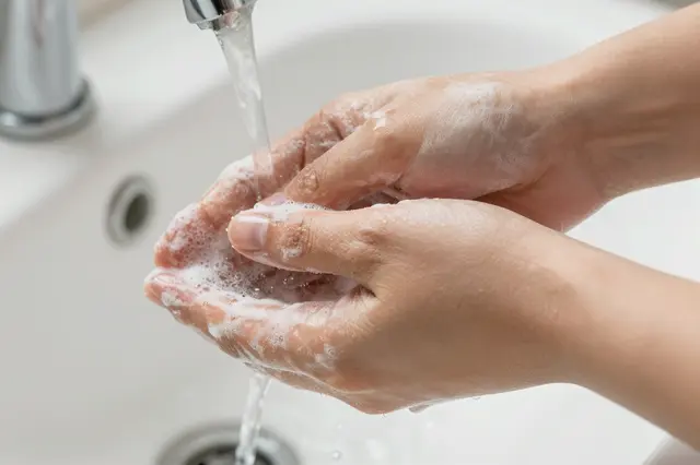 Close up of soapy human hands being rinsed under running tap water over a bathroom sink
