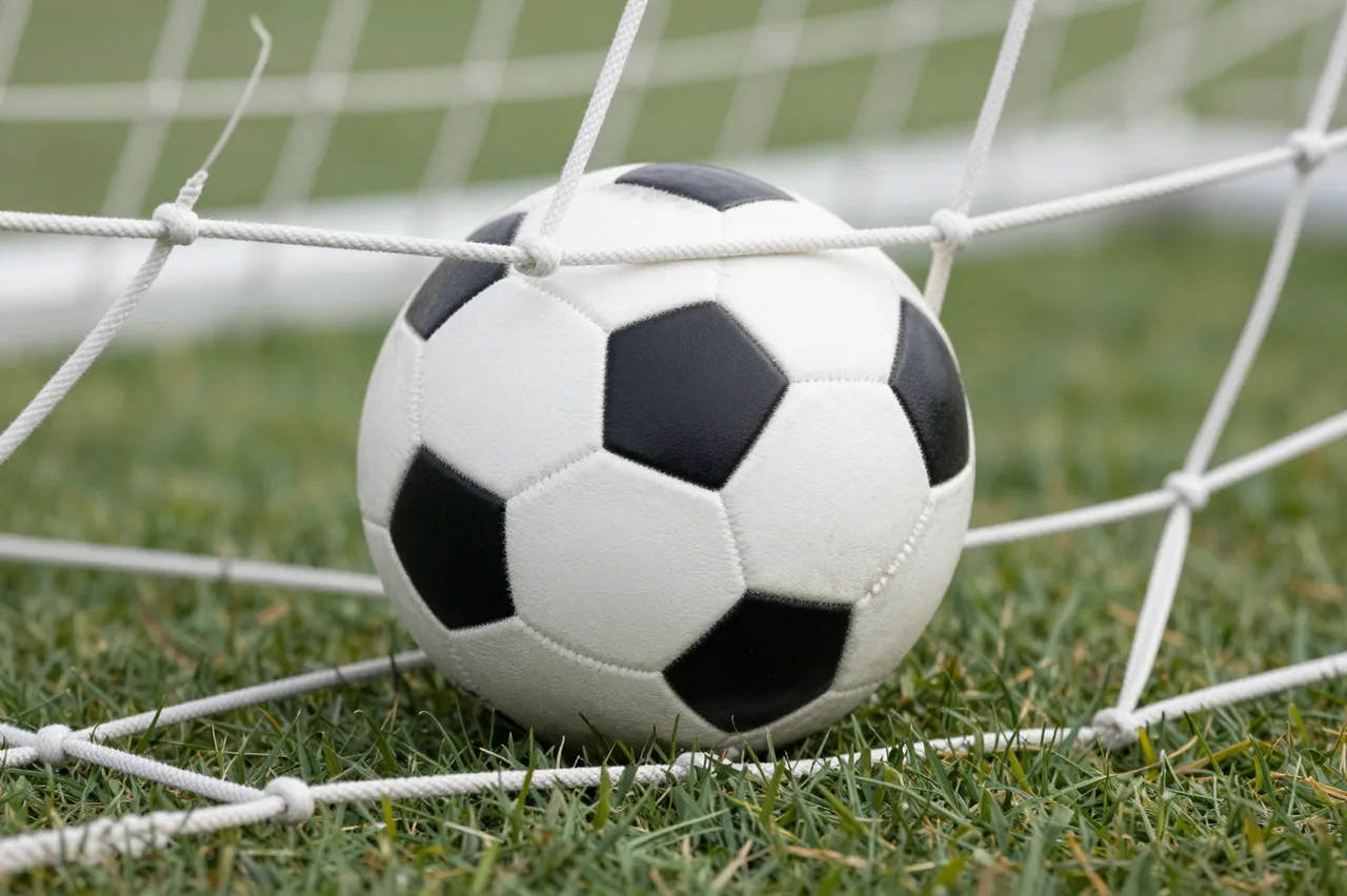 A classic black and white soccer ball rests against the goal net on green grass.
