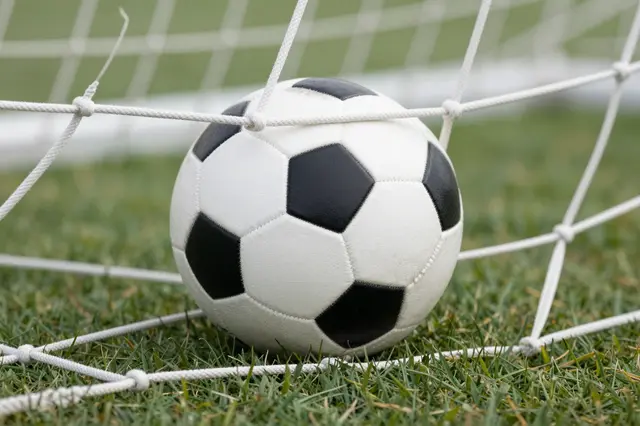 A classic black and white soccer ball rests against the goal net on green grass.