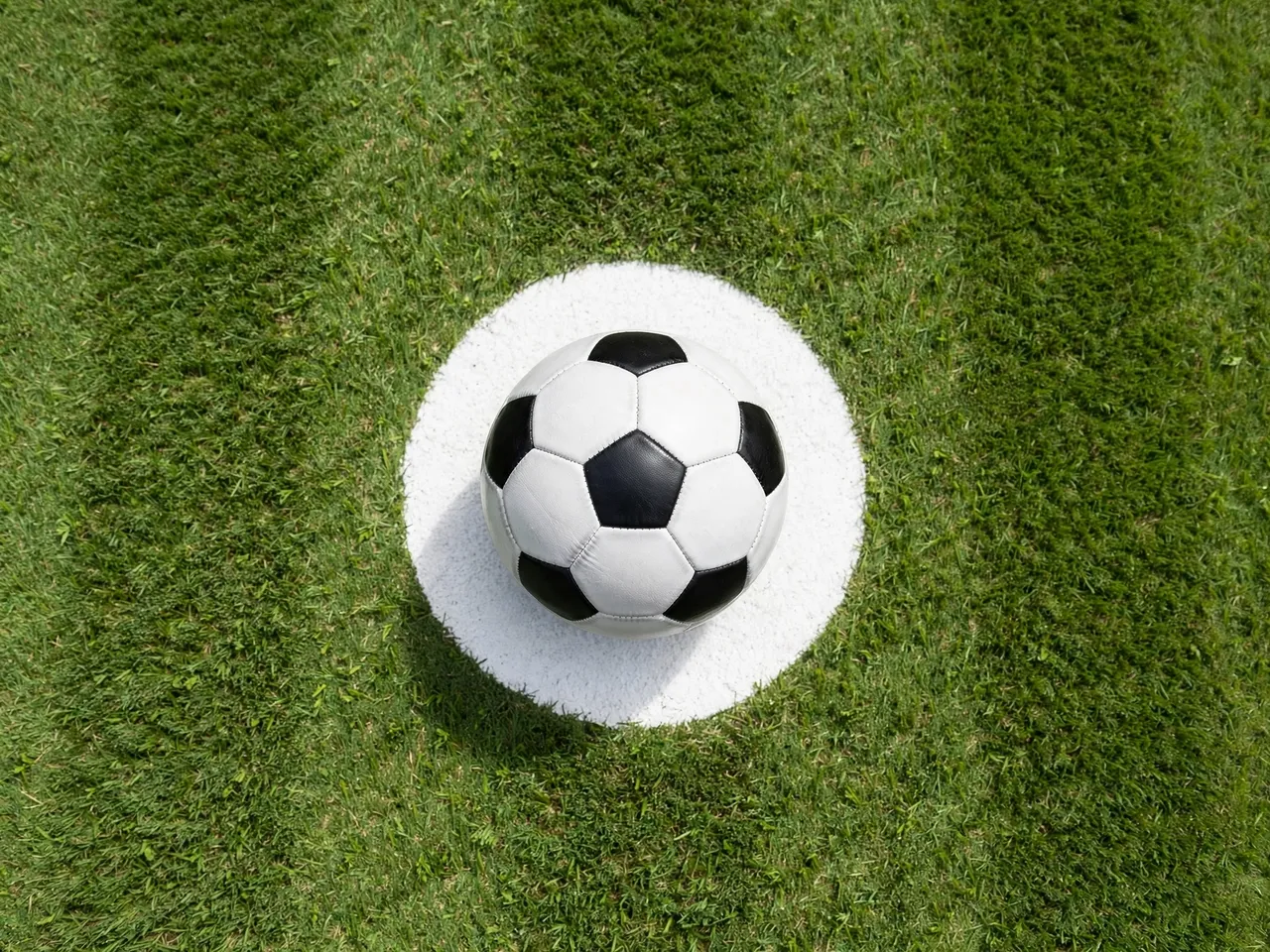 Overhead view of a classic black and white soccer ball resting on the white center circle of a mown grass soccer pitch