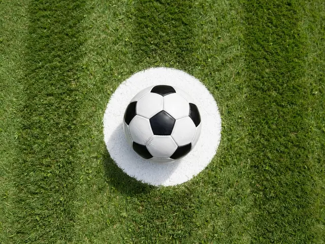 Overhead view of a classic black and white soccer ball resting on the white center circle of a mown grass soccer pitch