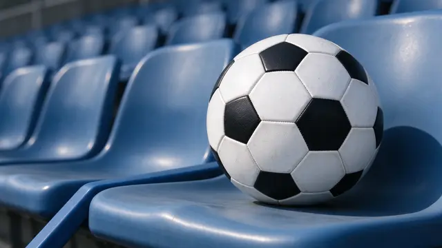 Classic black and white soccer ball resting on a blue plastic stadium seat with blurred empty seats behind