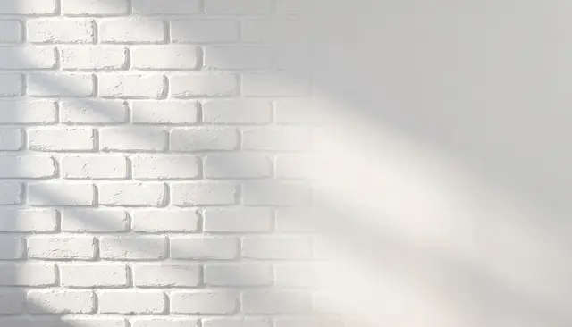 Painted white brick wall with soft left-side lighting and large blank right copy space