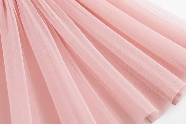 Close-up view of layered, flowing soft pink tulle fabric arranged in gentle diagonal folds