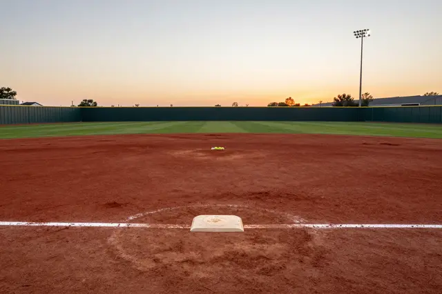 Empty softball field with red dirt infield viewed from home plate at golden sunset