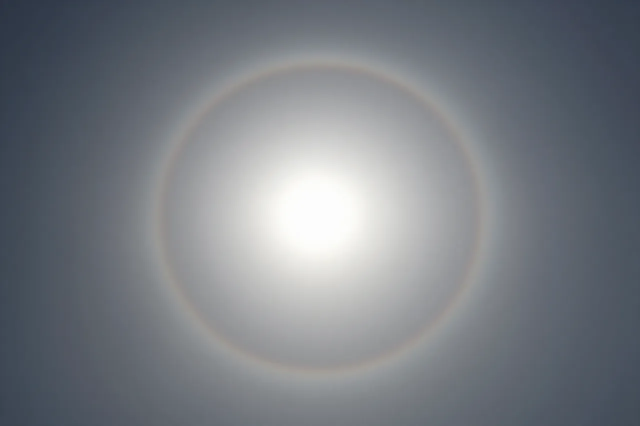 A bright solar halo forms around the sun viewed through thin hazy high clouds