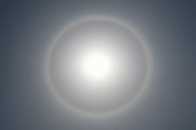 A bright solar halo forms around the sun viewed through thin hazy high clouds