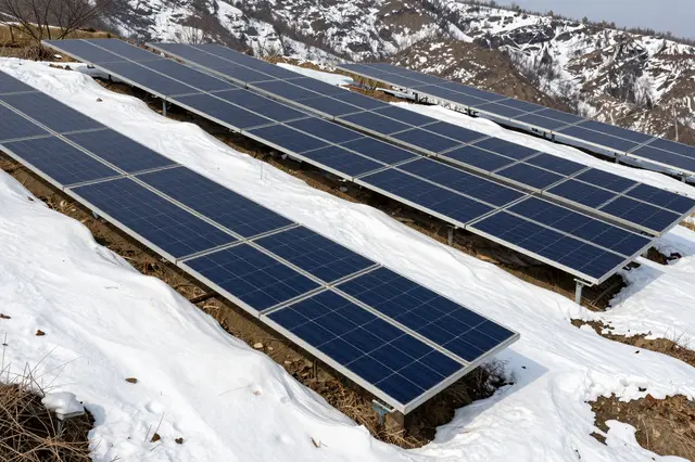 Rows of solar panels mounted on a snowy mountain slope with rocky snow-dusted peaks in the background