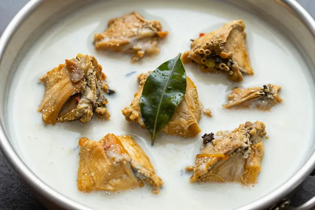 Pan of creamy coconut milk chicken curry garnished with a fresh curry leaf