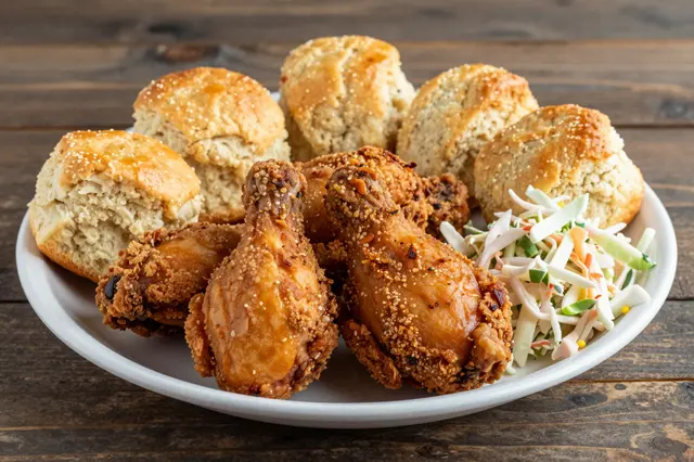 A white platter of crispy fried chicken, buttermilk biscuits and coleslaw sits on a rustic dark wooden table