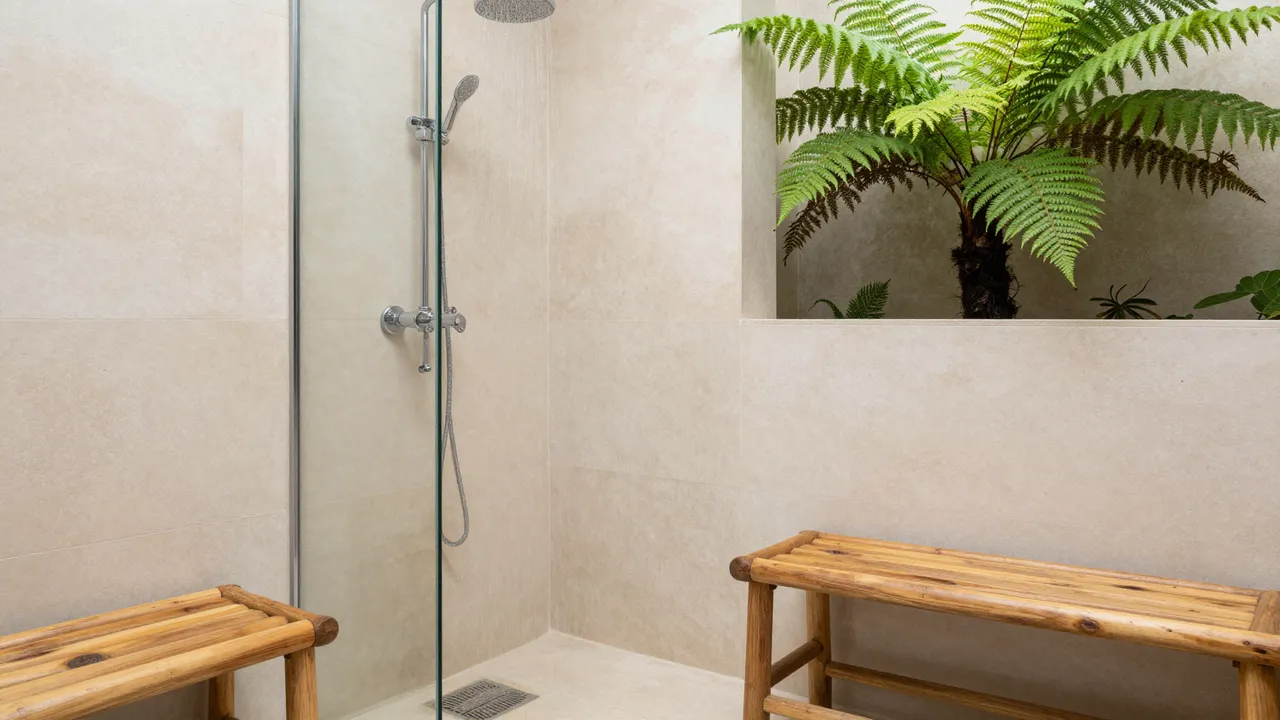A tiled spa shower with teak benches opens to a built-in niche holding a large fern plant