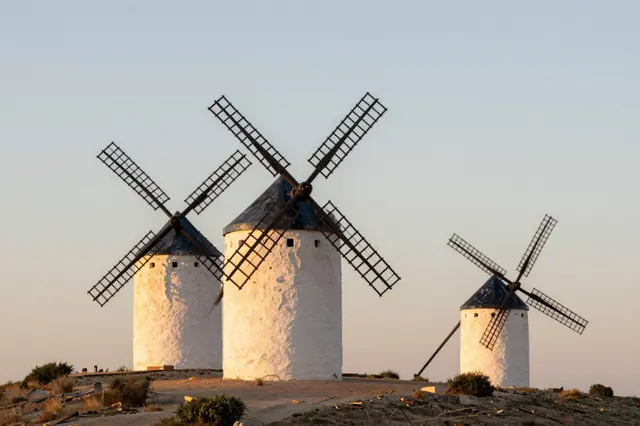 Three traditional white stone windmills stand on a dry sunlit ridge at golden sunset