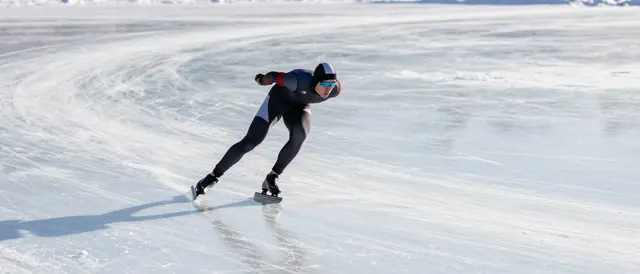 An adult speed skater leans into a turn gliding across a vast sunlit frozen lake