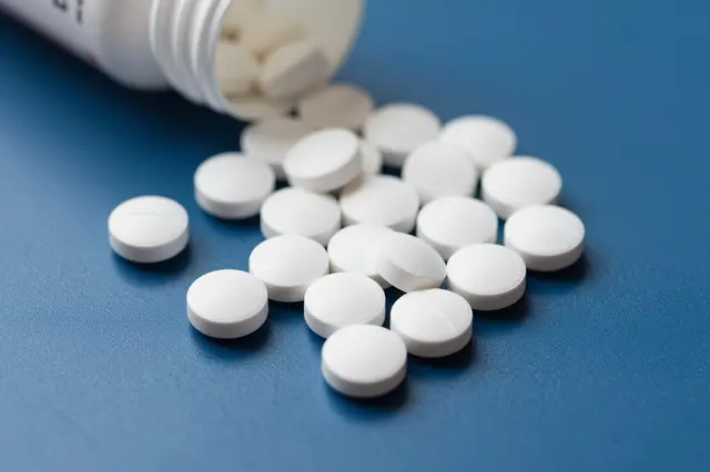 A tipped white pill bottle spills round white tablets across a smooth deep blue surface.