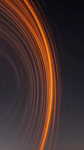 Curved orange long-exposure light trails arc across a dark starry night sky
