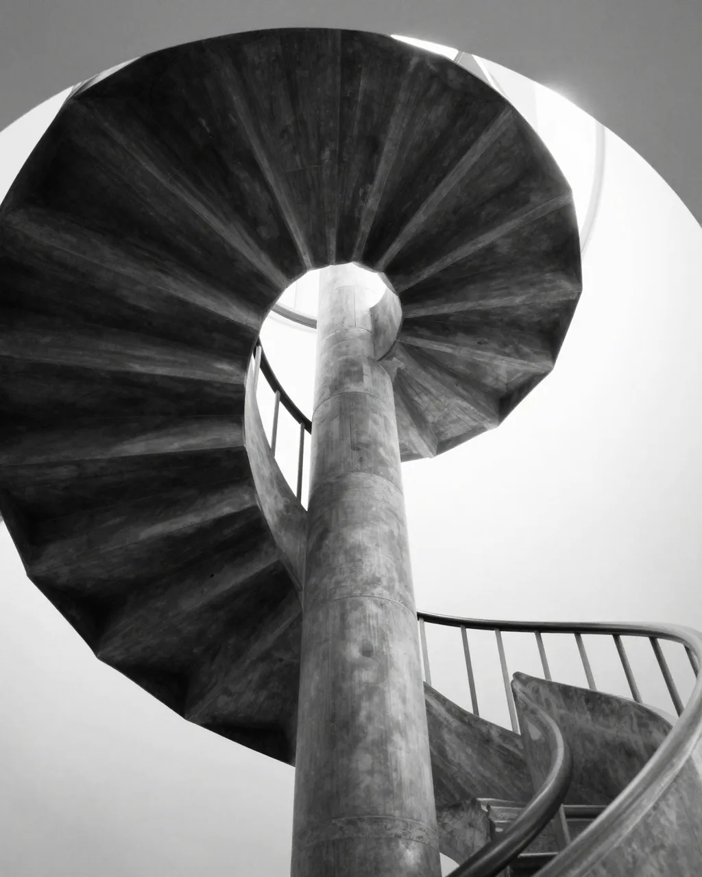 Low angle black and white view of a concrete spiral staircase looking upward from its base