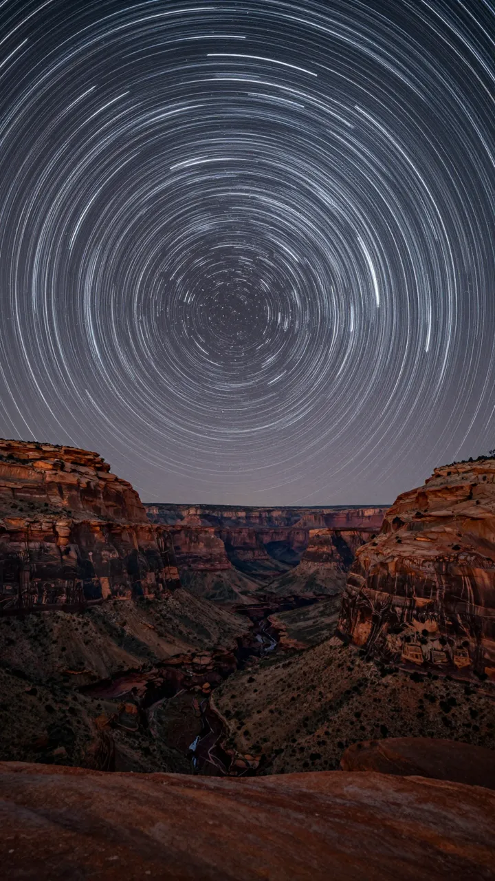 Circular long exposure star trails arc above a rugged red rock canyon at night