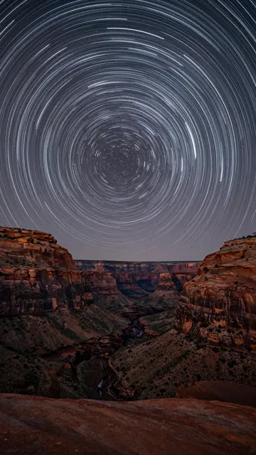 Circular long exposure star trails arc above a rugged red rock canyon at night