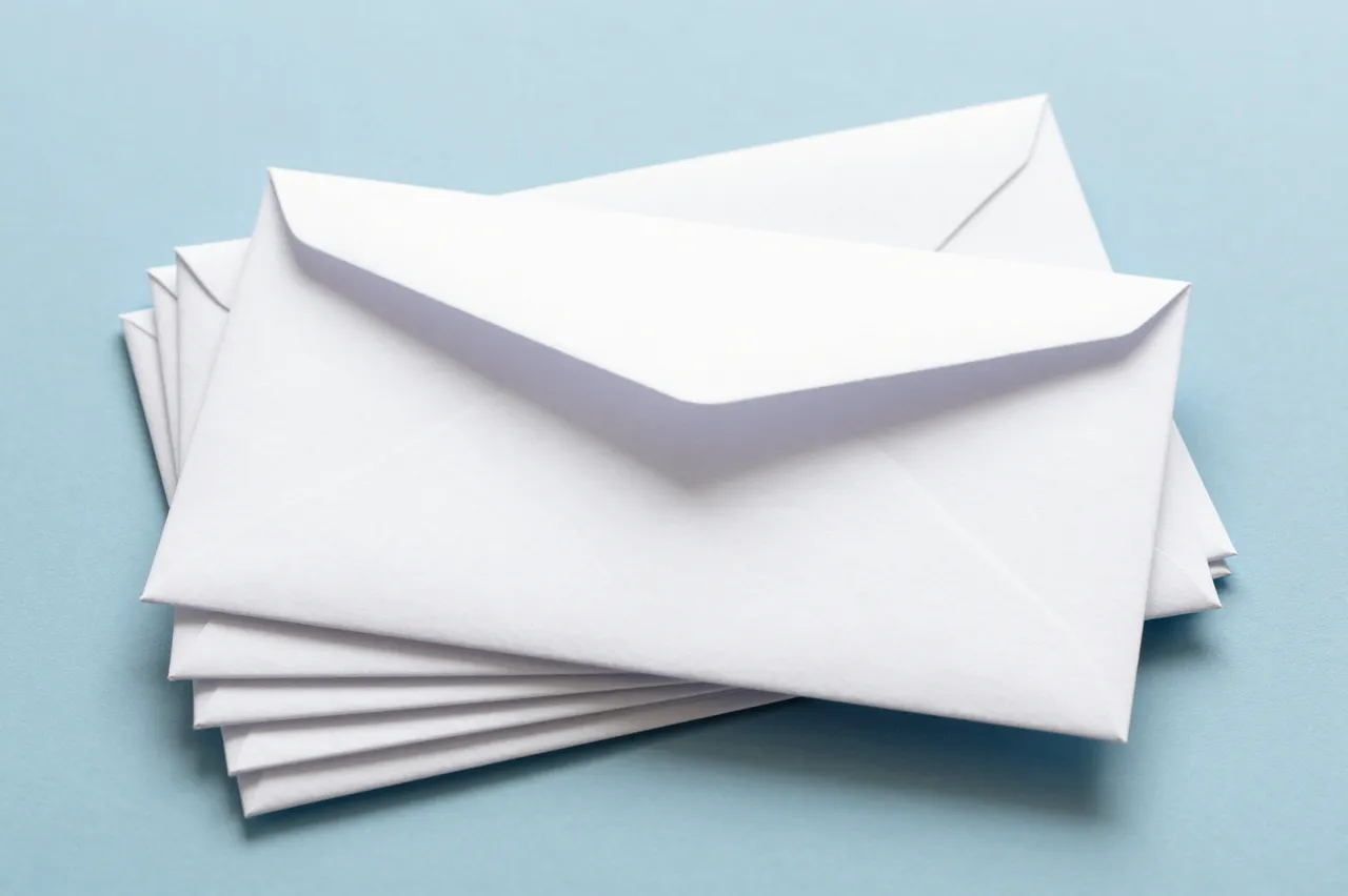 A stack of plain white envelopes rests on a smooth pale blue background, with the top envelope slightly open.
