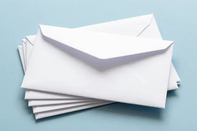A stack of plain white envelopes rests on a smooth pale blue background, with the top envelope slightly open.