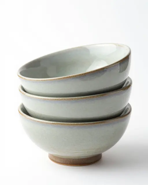 Three stacked speckled glazed ceramic bowls sit isolated on a plain white studio background.