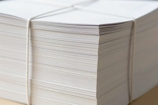 Close-up of a thick stack of plain white paper secured with thin string resting on a light surface