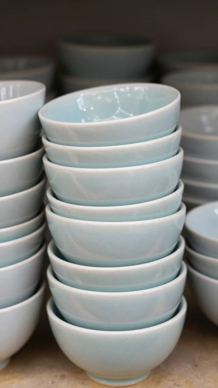 Neat stacks of glossy muted pale blue ceramic bowls arranged on a neutral textured surface