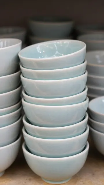 Neat stacks of glossy muted pale blue ceramic bowls arranged on a neutral textured surface