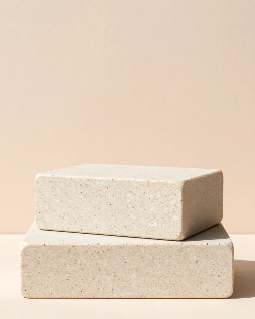 Two stacked travertine blocks rest on a pale peach backdrop with soft side daylight