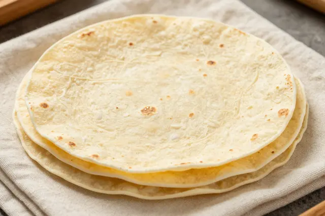 A stack of fresh warm flour tortillas rests on a folded linen cloth