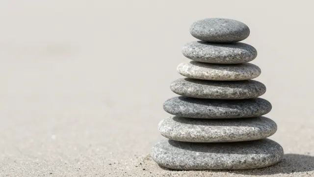 A balanced stack of smooth gray stones sits on pale sand with empty copy space to the left