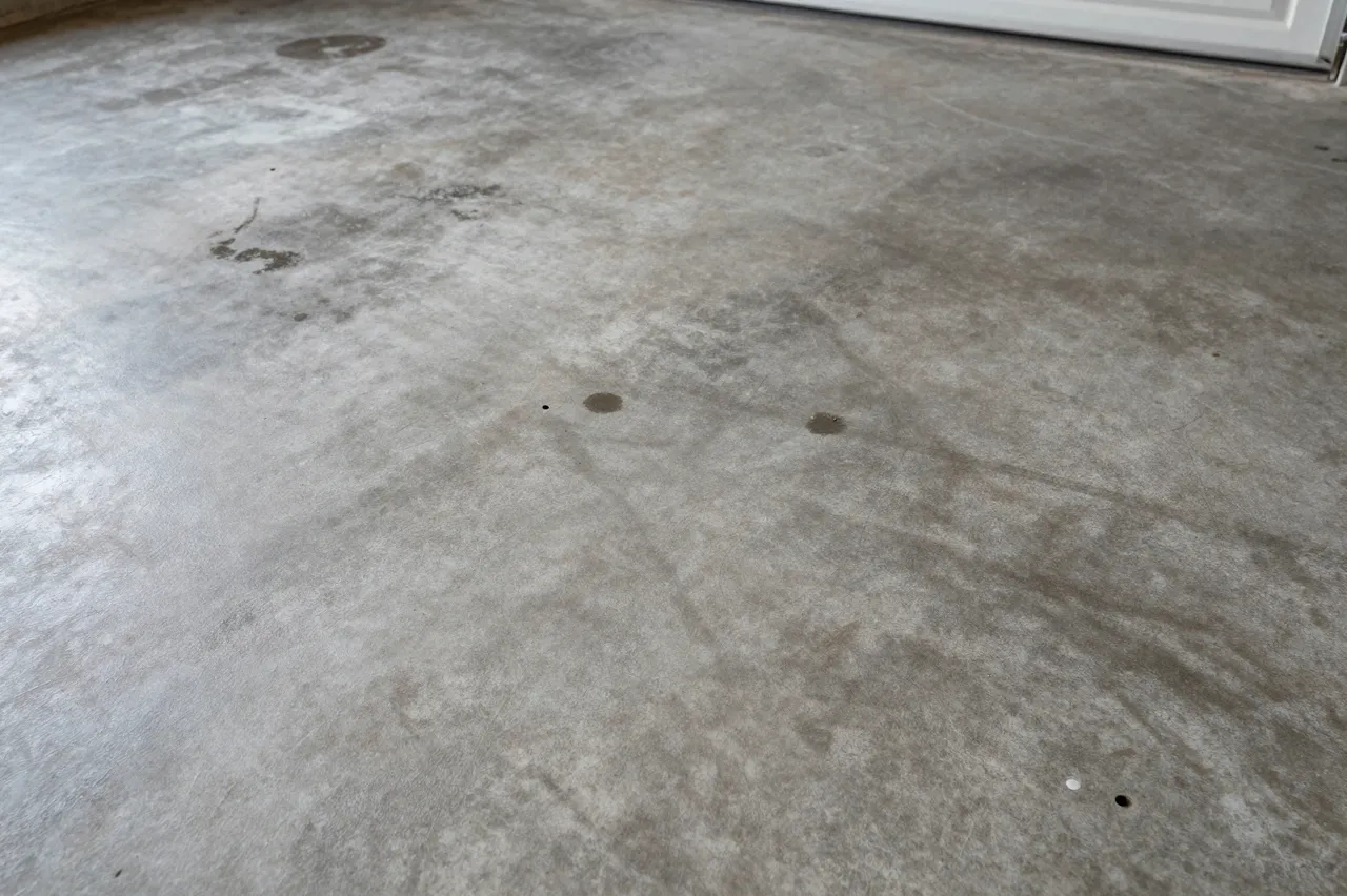 Top view of a worn concrete garage floor marked with dark oil stains and scuff marks under flat lighting