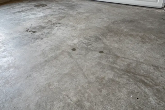 Top view of a worn concrete garage floor marked with dark oil stains and scuff marks under flat lighting