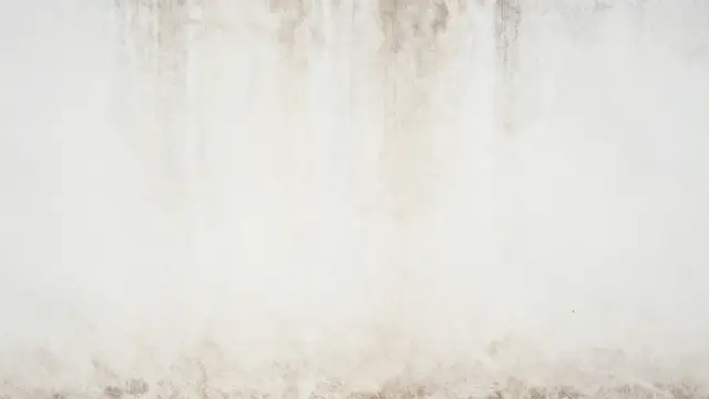 Full frame close up of a worn white plaster wall with faint vertical brown stains and rough grunge texture