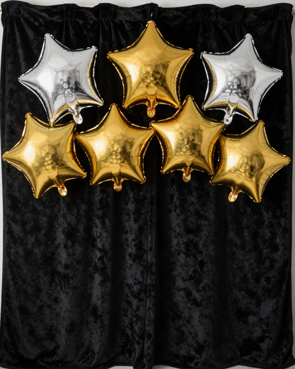 Gold and silver star-shaped foil balloons hang against a black velvet curtain with empty space below.
