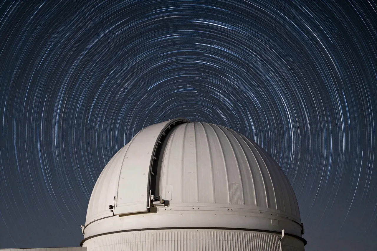 Long exposure circular star trails arc across a dark night sky above a white observatory dome.