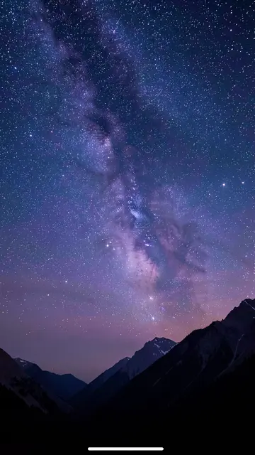 A dense starry milky way sky hangs over dark silhouetted mountain peaks at twilight.