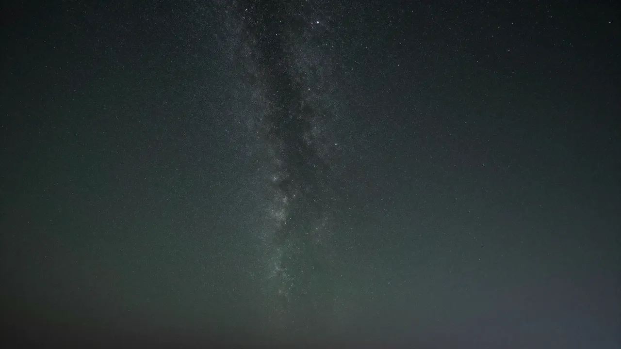 A dark night sky dotted with countless stars and a vertical Milky Way band above faint green horizon airglow