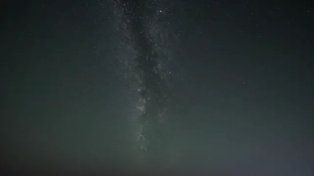 A dark night sky dotted with countless stars and a vertical Milky Way band above faint green horizon airglow