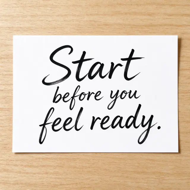 Handwritten quote "Start before you feel ready." in black ink on a white index card resting on a light wooden desk