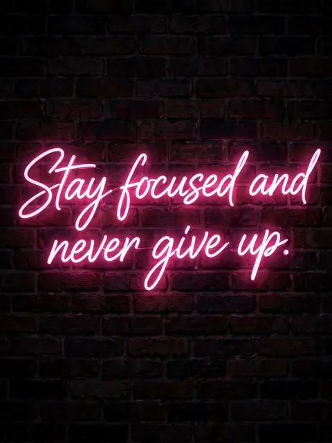 Glowing pink neon sign reading "Stay focused and never give up." mounted on a dark nighttime brick wall
