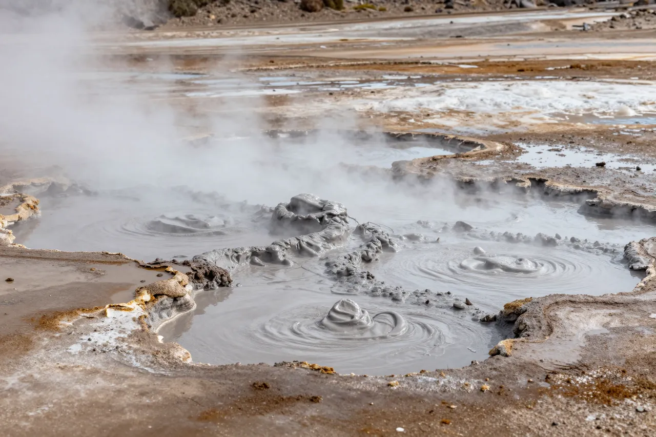 Bubbling gray mud pools emit steam across a rocky geothermal field