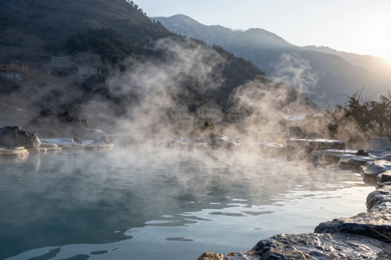 Steam rises from a mountain hot spring pool as golden sunrise light hits distant forested peaks