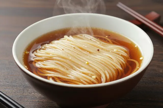 A hot steaming bowl of thick noodles in broth sits on a dark wooden counter with chopsticks beside it.