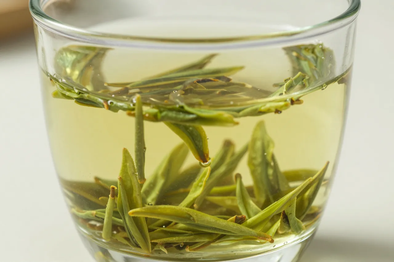 Close-up of a glass cup holding pale green brewed tea with unfurling loose tea leaves.