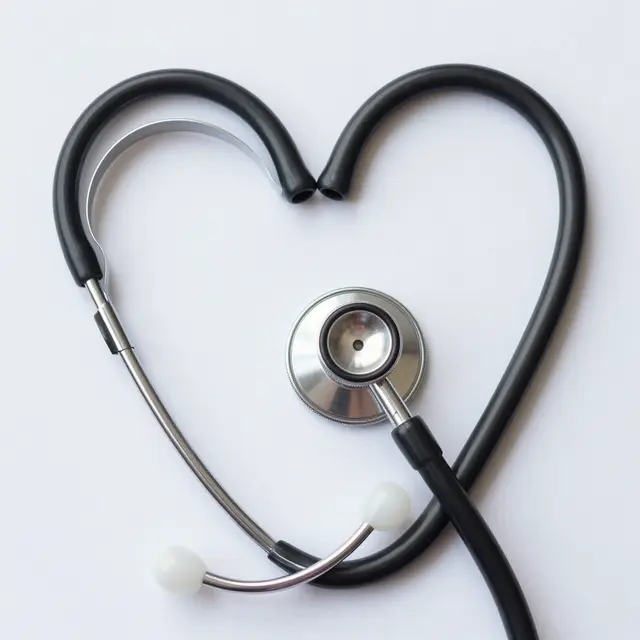 A top-down view of a stethoscope arranged into a heart shape on a plain white surface