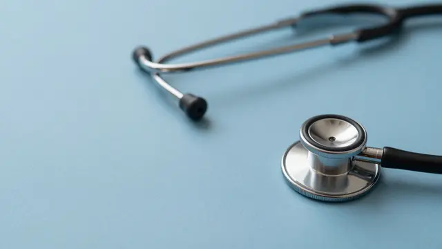 A stethoscope rests at the edge of a smooth pale blue surface with wide empty copy space.